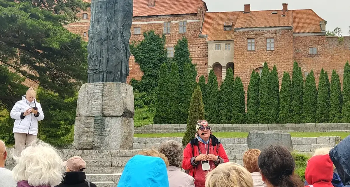 Grupa turystów słucha przewodnika przy pomniku Kopernika. To jedna z wielu atrakcji Warmii, gdzie historia ożywa.