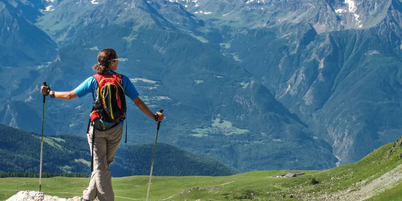Donna con zaino e bastoncini da trekking ammira i maestosi **sentieri Valle d'Aosta** e le cime innevate.