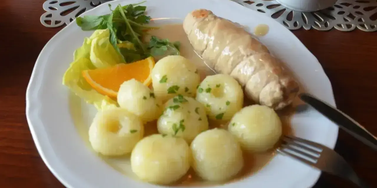 Pyszne kluski śląskie z roladą mięsną, surówką z czerwonej kapusty i plasterkiem pomarańczy.