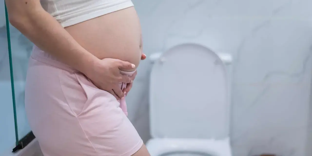 Ciąża to piękny czas, ale czasem pojawia się popuszczanie moczu. Kobieta w ciąży w łazience, obok toalety.