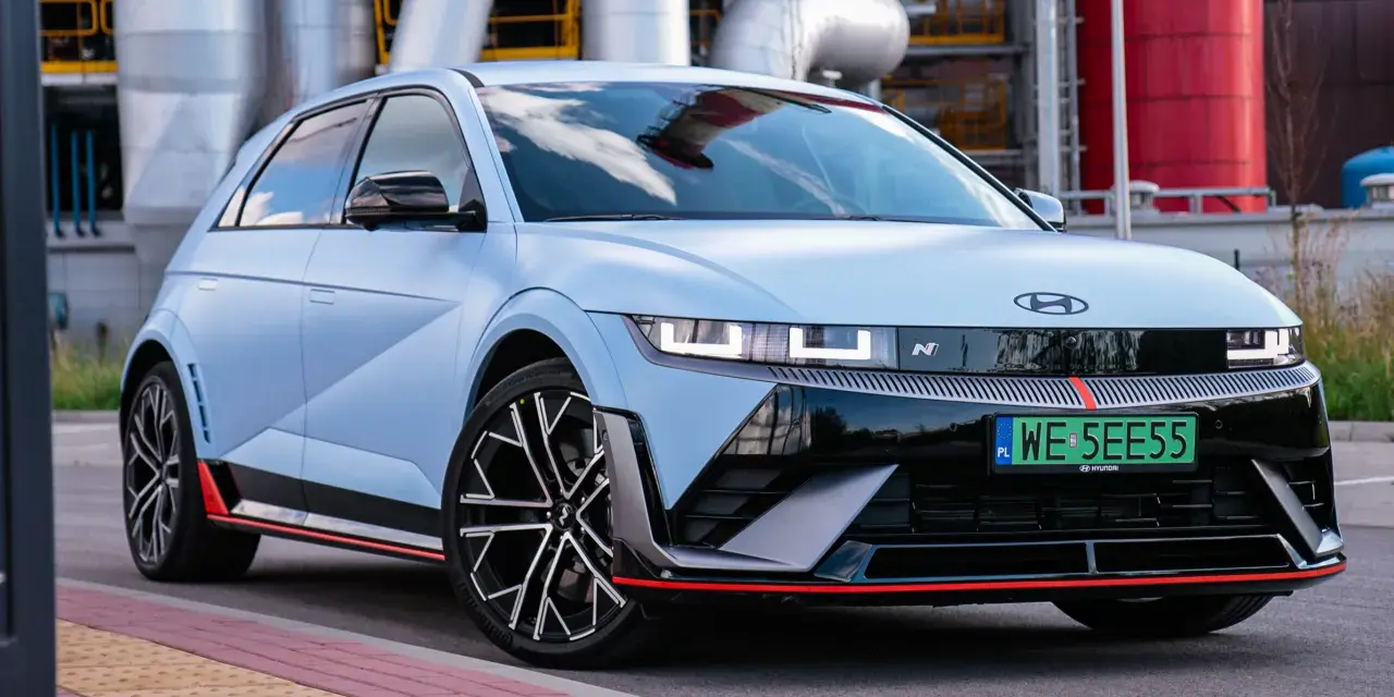 Jasnoniebieski Hyundai IONIQ 5 N z czarnymi akcentami i czerwonymi detalami, zaparkowany przed przemysłową instalacją.