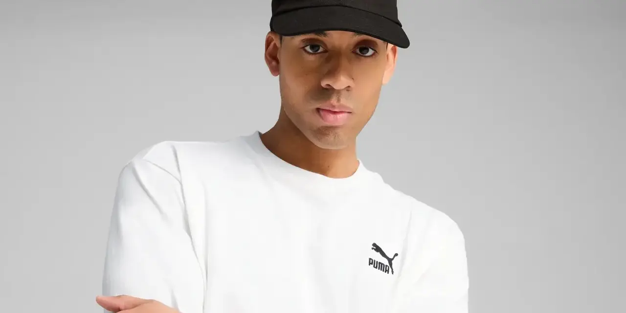 Mężczyzna w czarnej czapce z logo Puma i białej koszulce.