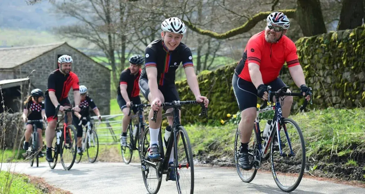 Un groupe de cyclistes souriants roule sur une route de campagne, respectant le code de la route pour cycliste en groupe.