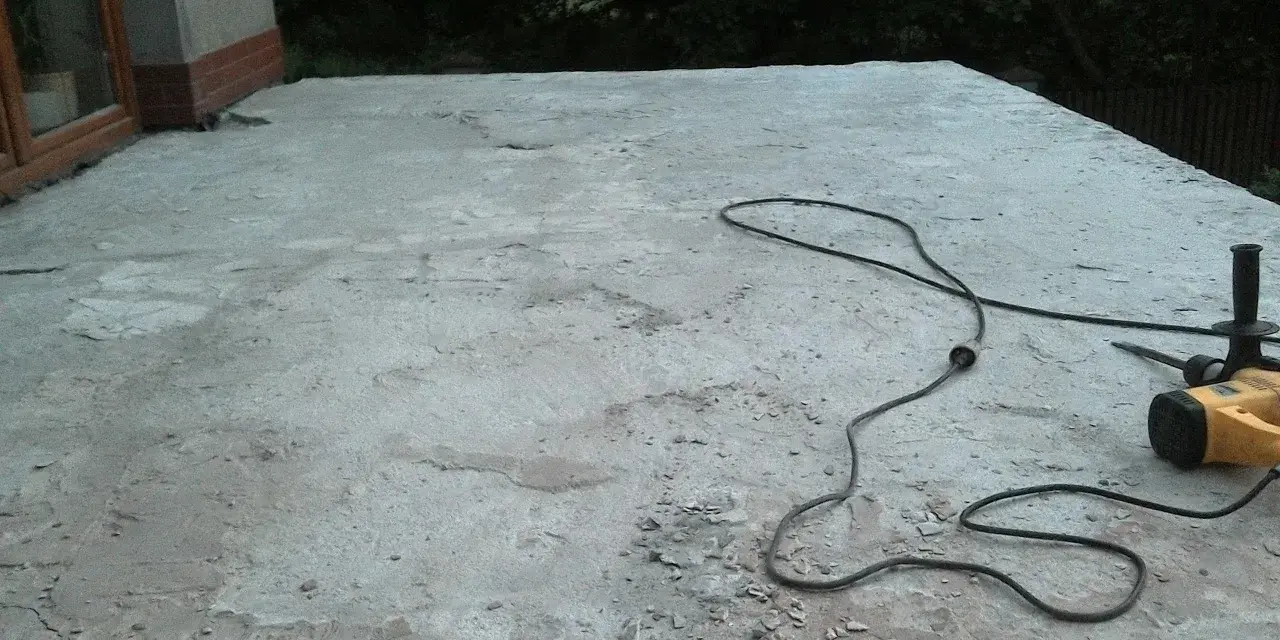 Betonowy taras czeka na remont. Obok leży młot udarowy, gotowy do pracy. Nivoplan pomoże w pracach.