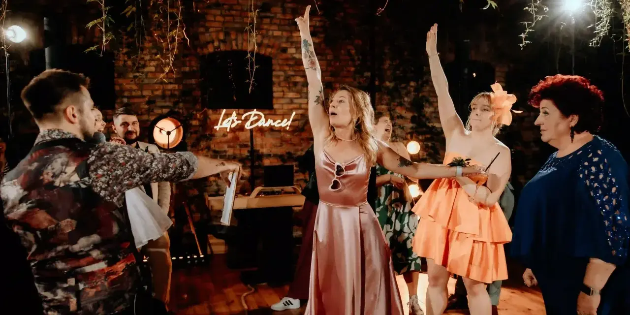 Wesele w pełni! Neon "Let's Dance!" i kobiety w sukniach unoszą ręce. Świetny pomysł na oczepiny i zabawę do białego rana.