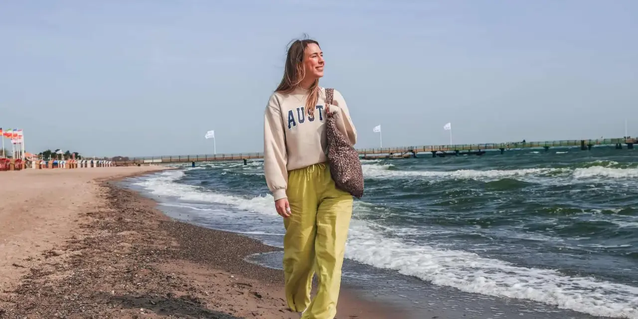 Frau spaziert am stein strand entlang, die Wellen rauschen.