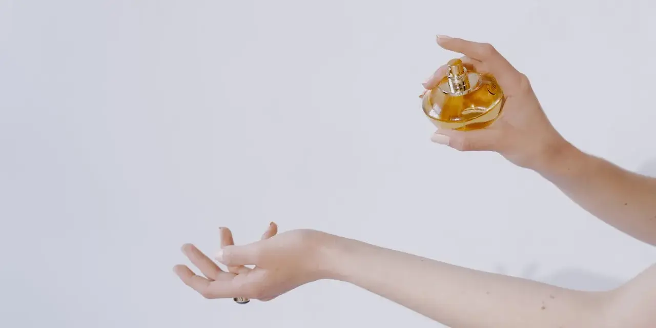 Dłoń trzymająca perfumy nad drugą dłonią.