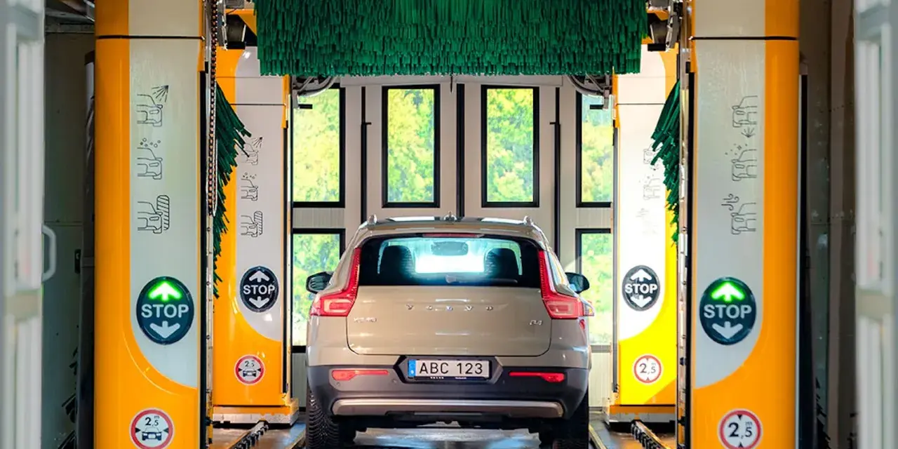 Volvo XC40 i en automatisk biltvätt med autoclean + wax-program. Gröna borstar hänger redo för en skinande ren bil.
