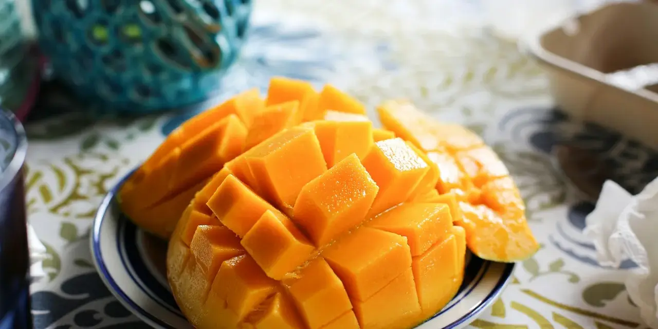 En skål med skivad mango, full av vitaminer, på en duk med mönster.
