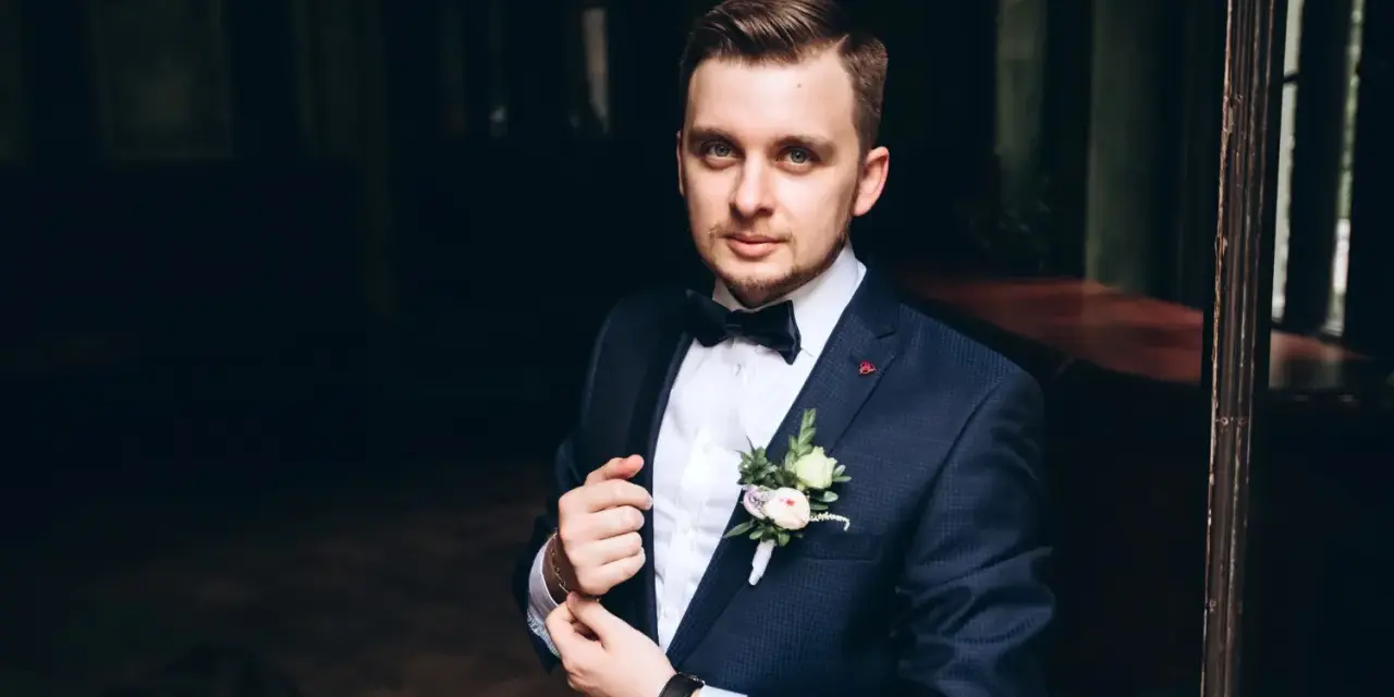 Elegancki mężczyzna w granatowym smokingu z kamizelką, z butonierką.