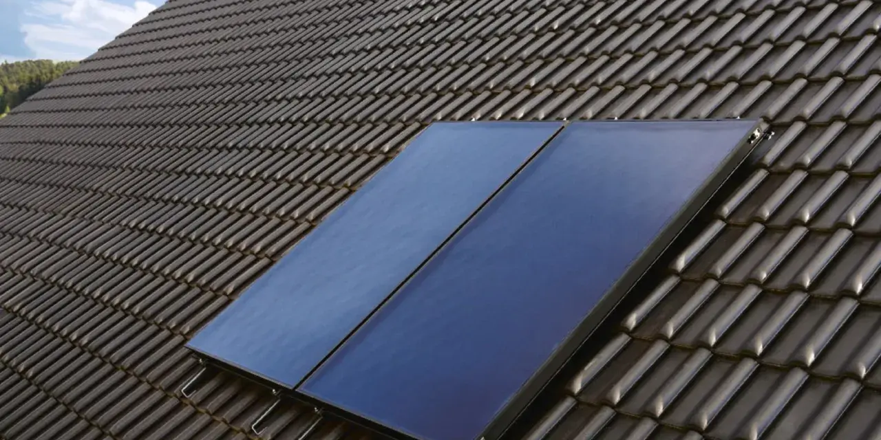 Deux panneaux de chauffage solaire thermique installés sur un toit en tuiles sombres, sous un ciel bleu.