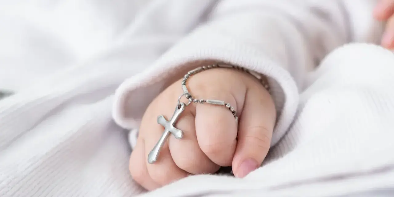 Dziecięca rączka z krzyżykiem na bransoletce. Symboliczny prezent, ile daje się na chrzciny.
