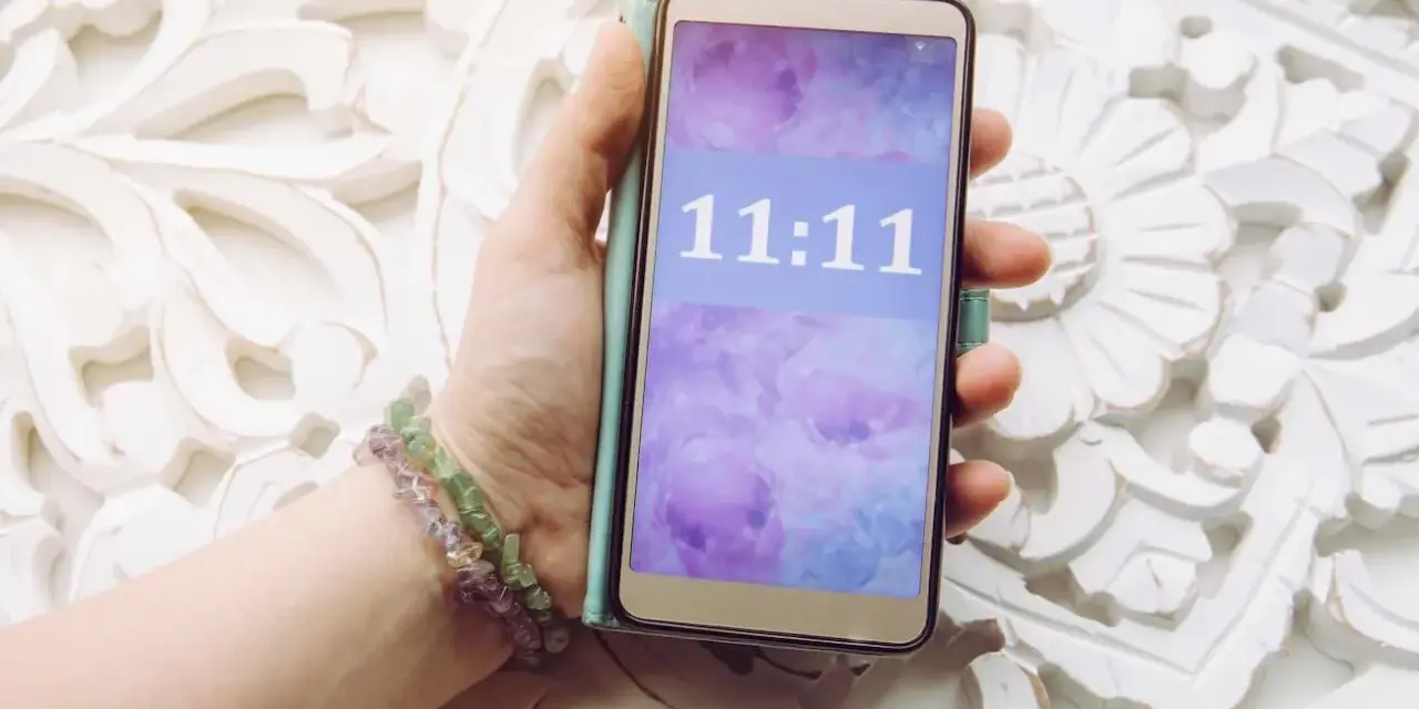 Dłoń trzyma telefon z wyświetloną godziną 11:11, co może mieć szczególne znaczenie.