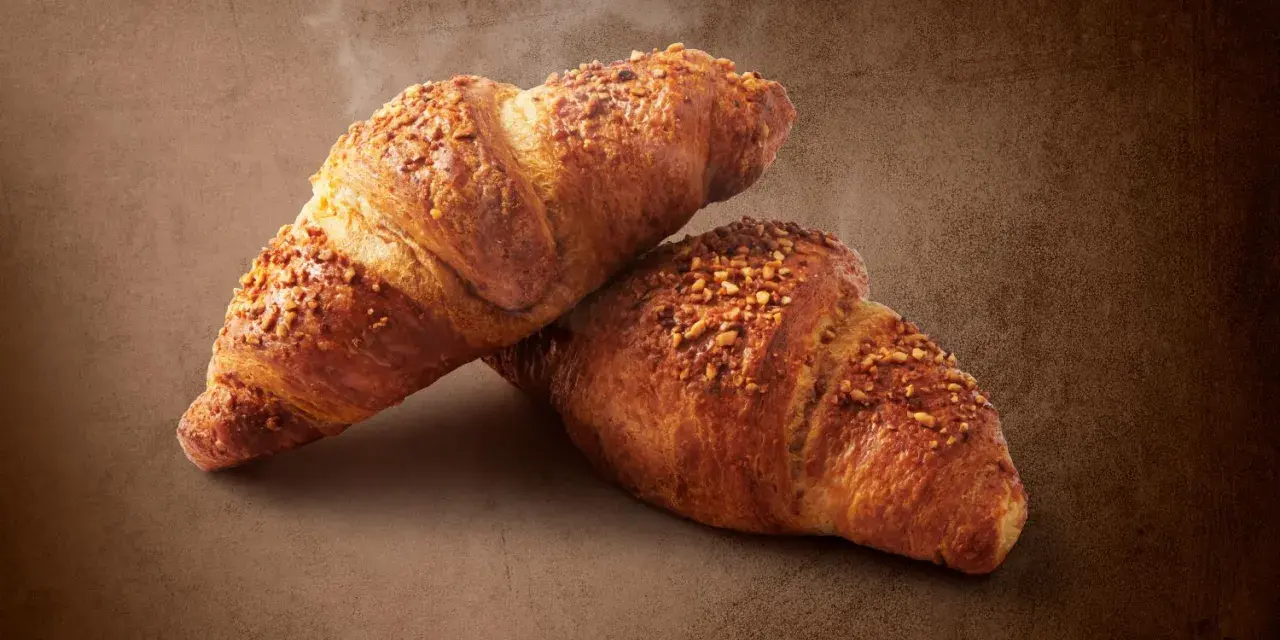 Dwa chrupiące croissanty posypane orzechami. Pyszna przekąska, ale warto pamiętać o ich kaloryczności - croissant kcal.