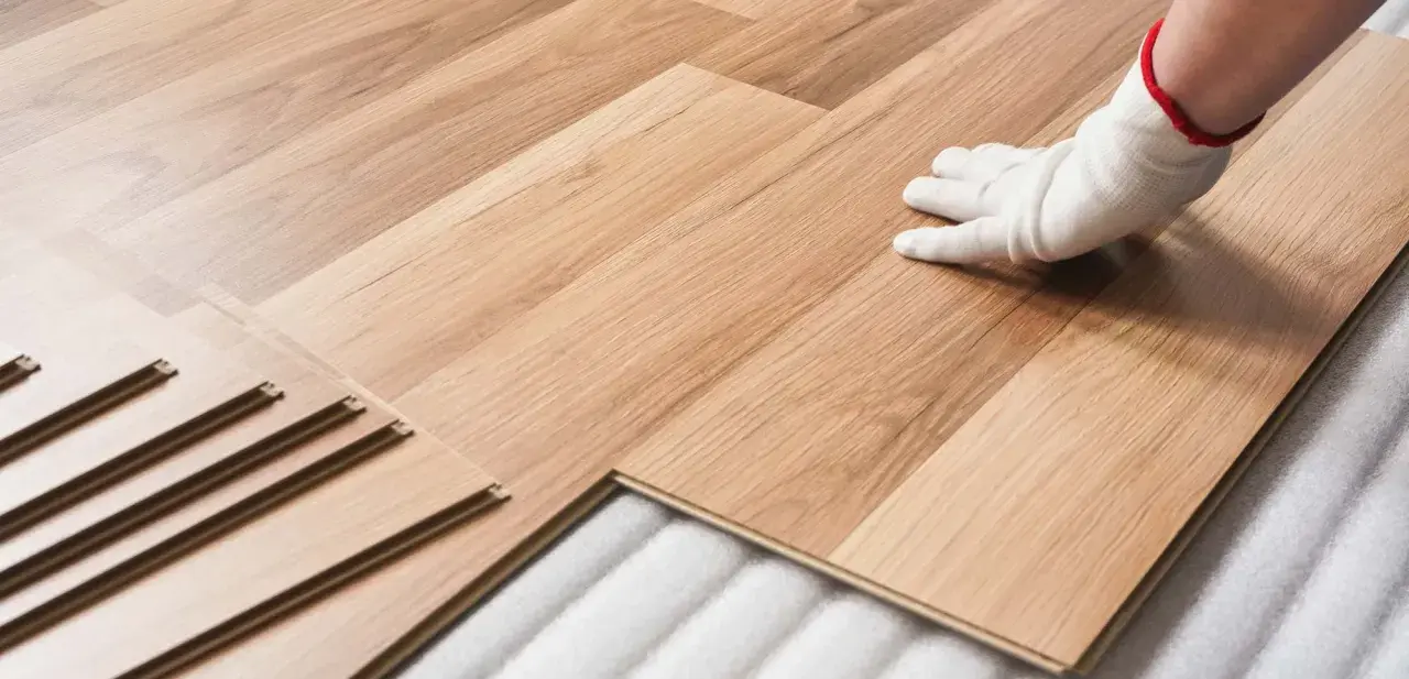 Instalación de suelo laminado. Mano con guante blanco colocando una tabla. Consulta el precio colocacion suelo laminado.