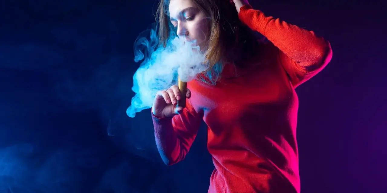 Joven exhala humo azul de un vaper. El vaper con nicotina es malo para la salud.