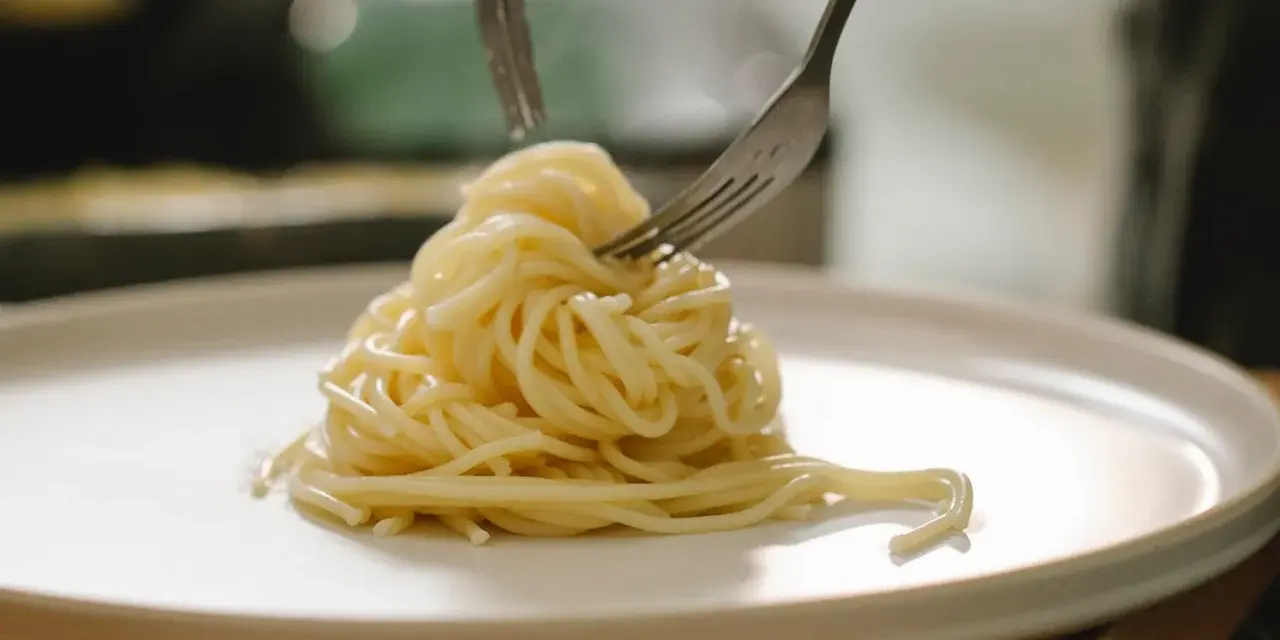 Spaghetti al limone cremosi serviti su un piatto bianco, con due forchette che li raccolgono.