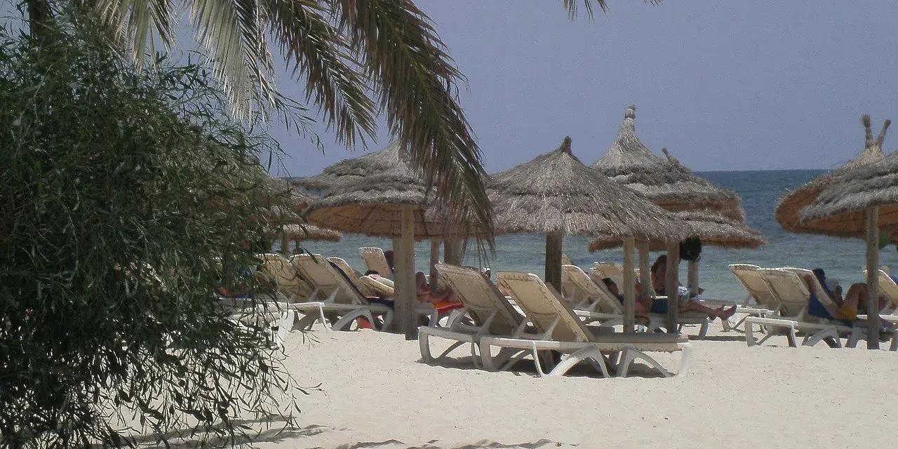 Plaża na Djerbie z leżakami i parasolami. Ludzie odpoczywają, co sugeruje, że na Djerbie jest bezpiecznie.