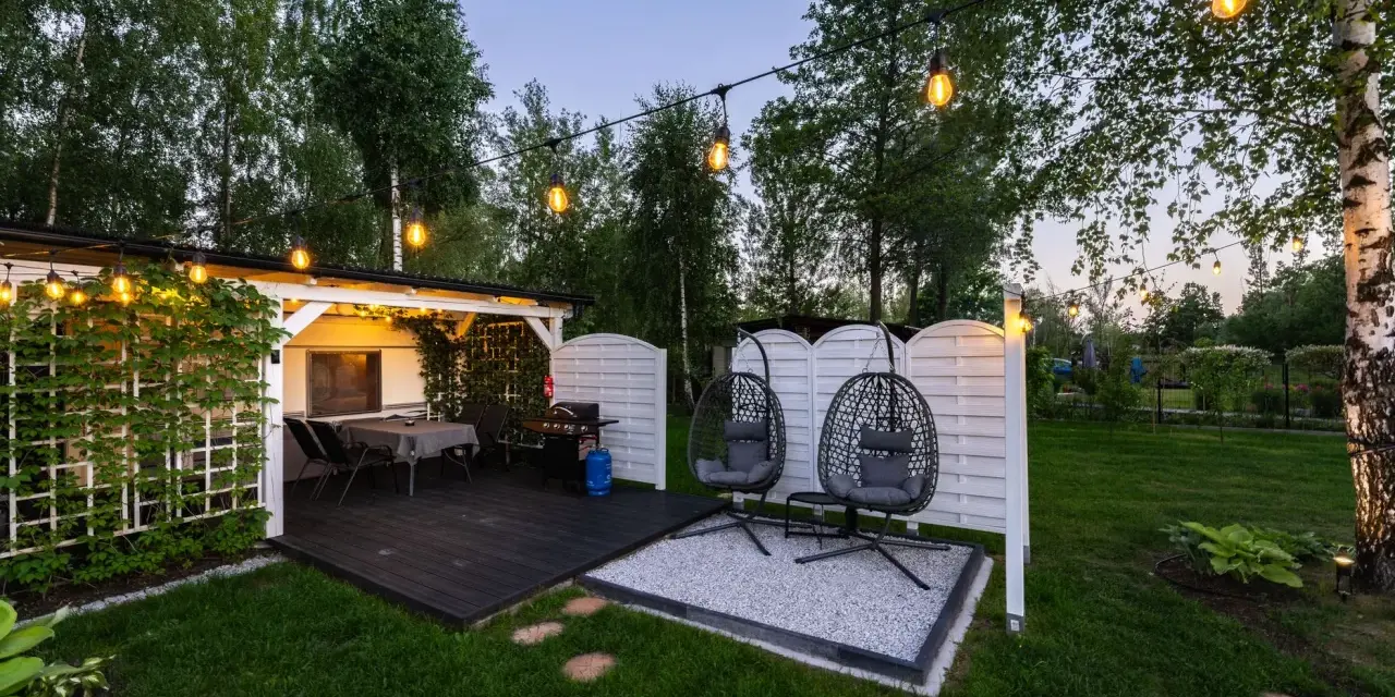 Idealne miejsce na camping w Ochabach: zadaszony taras z grillem, stolikiem i wiszącymi fotelami. Wieczorem rozświetla go girlanda żarówek.
