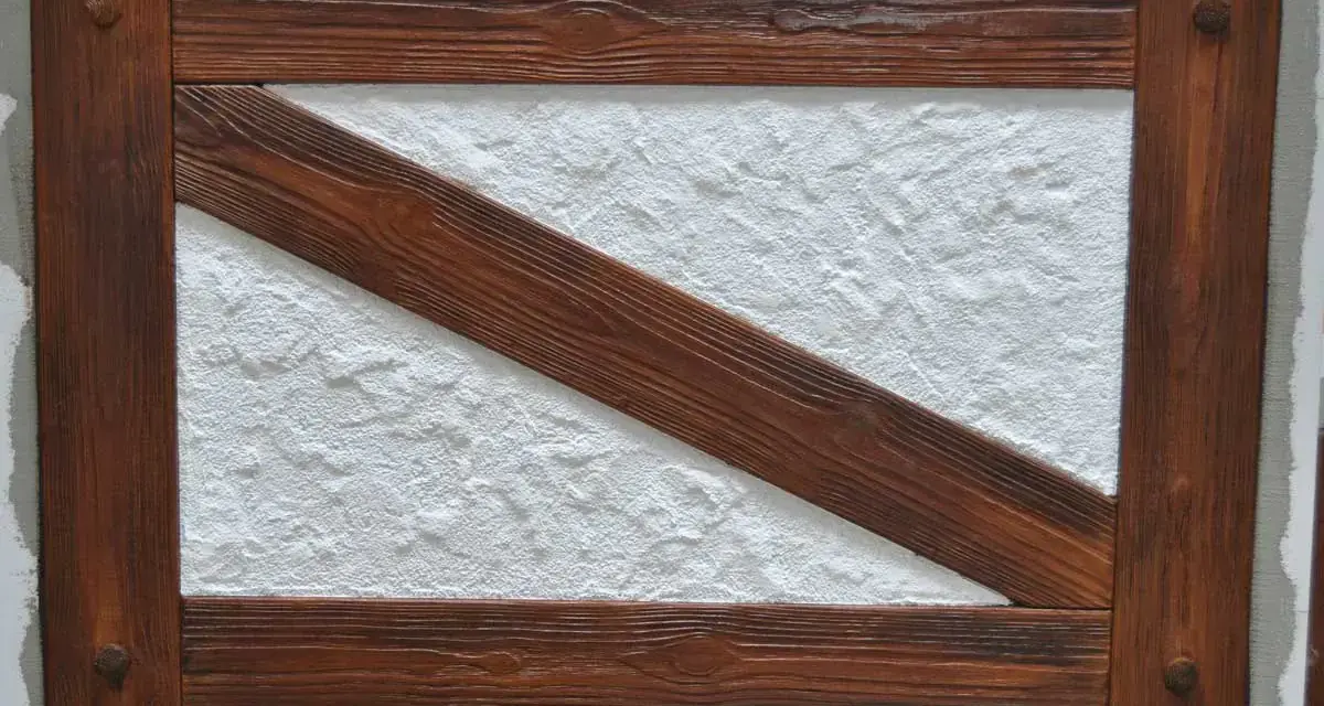 Drewniana rama imitująca mur pruski na elewacji, z białym, chropowatym tynkiem w środku.