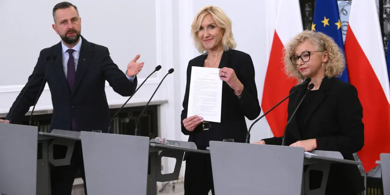 Trzy osoby przy mównicach, w tle flagi Polski i UE. Wibracja związku 8.