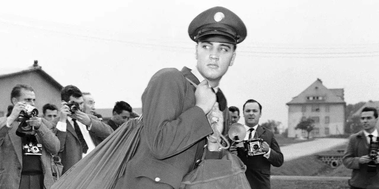 Elvis Presley 1958, in Uniform, wird von Paparazzi umringt, die mit ihren Kameras auf ihn richten.