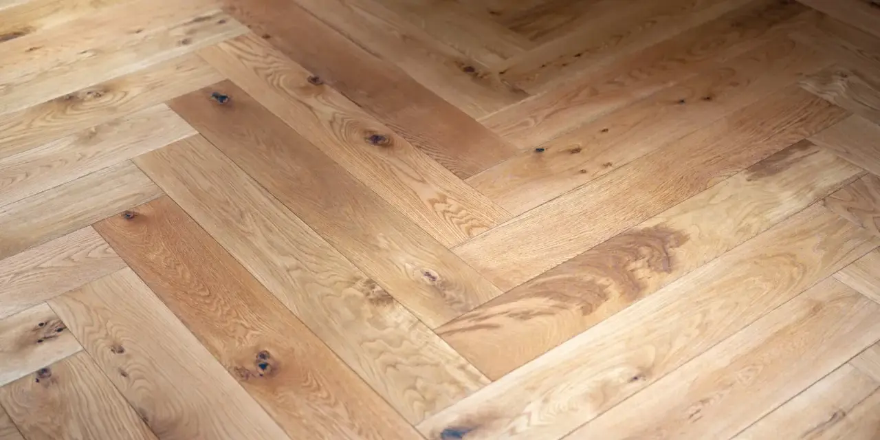 Tarima de madera en espiga, con nudos y vetas naturales, creando un patrón clásico y cálido.