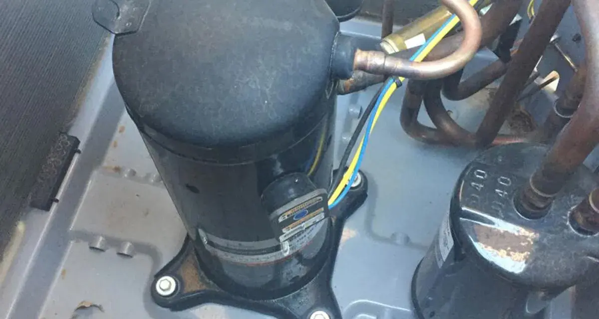 Close-up of an AC pump replacement in progress. A large black compressor sits on a gray base, connected to copper tubing and wires.