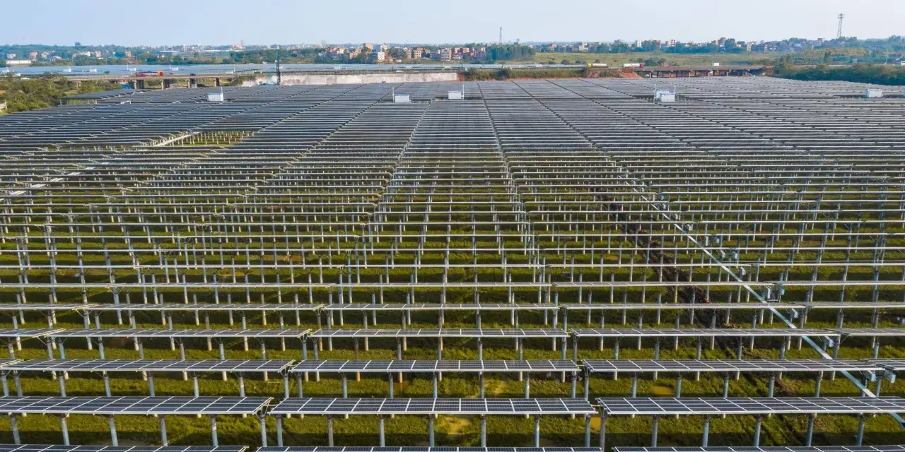 Ogromne połacie paneli fotowoltaicznych, część rozbudowy instalacji Tauron, na tle miejskiej zabudowy.