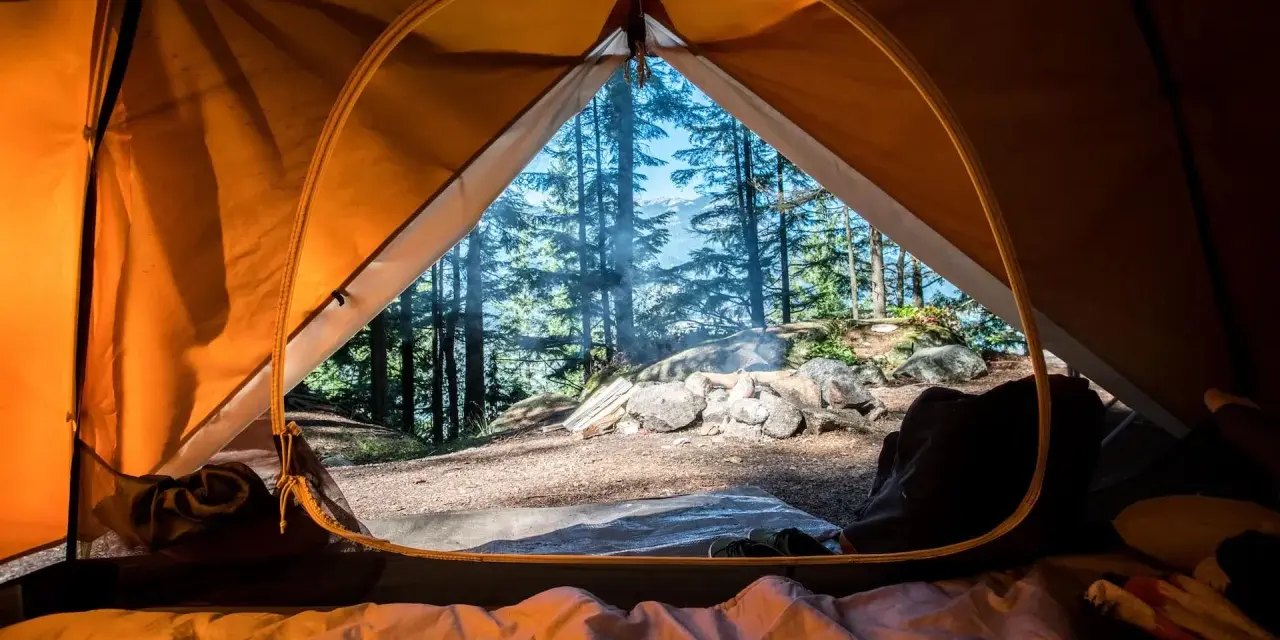 Vue de l'intérieur d'une tente orange, un feu crépite dehors. L'obligation sécurité camping est respectée avec ce campement bien installé.