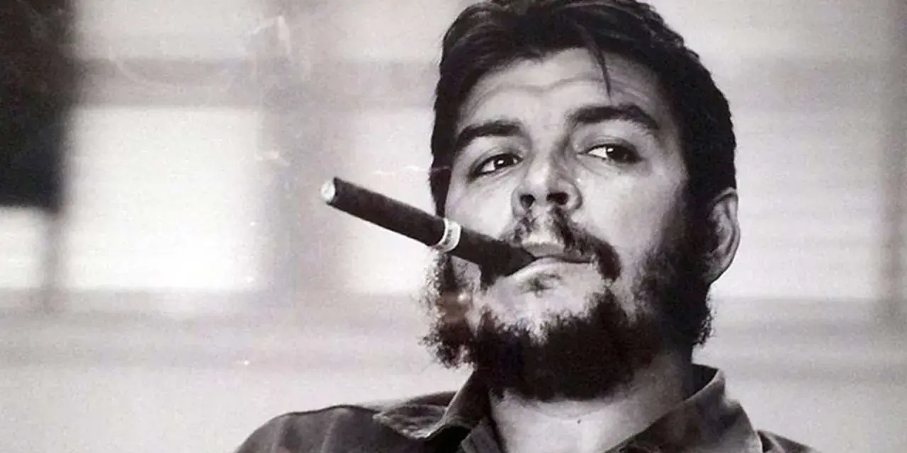 Portrait en noir et blanc de Che Guevara, cigare aux lèvres, regard intense. L'image évoque sa légende, même après sa mort.