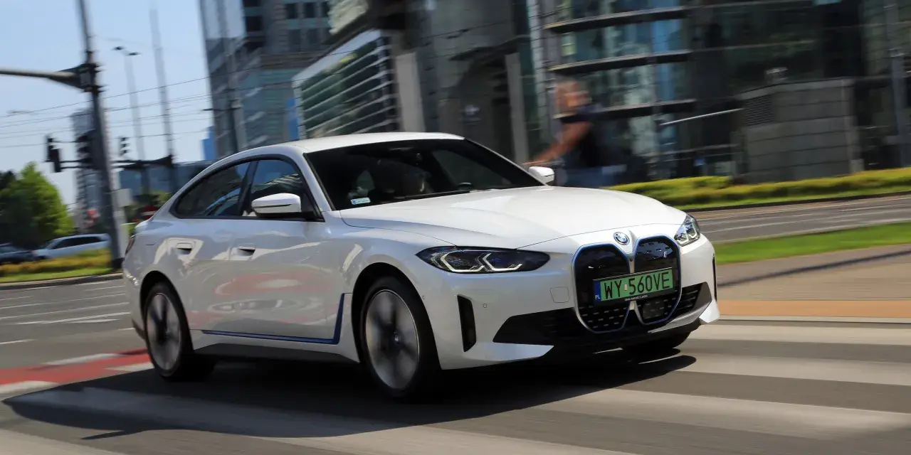 Białe BMW i4 w ruchu miejskim, z widocznymi światłami LED i grillem.