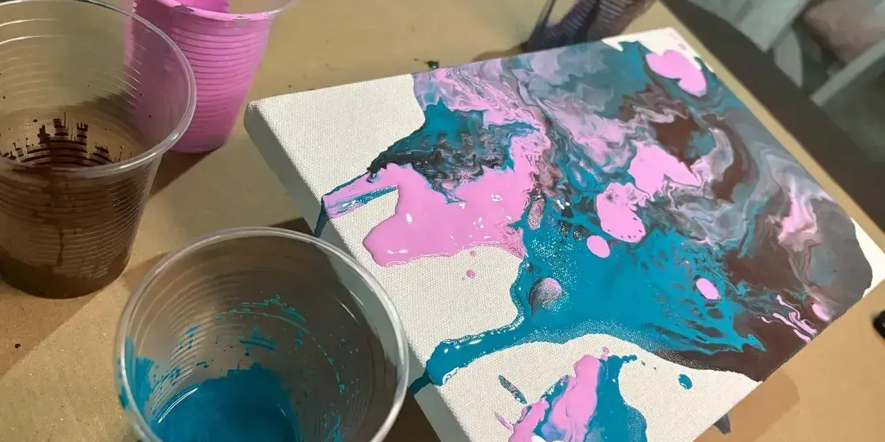 Peinture acrylique sur toile, avec des couleurs vives de rose, bleu sarcelle et marron qui coulent. Des gobelets en plastique contiennent les peintures.