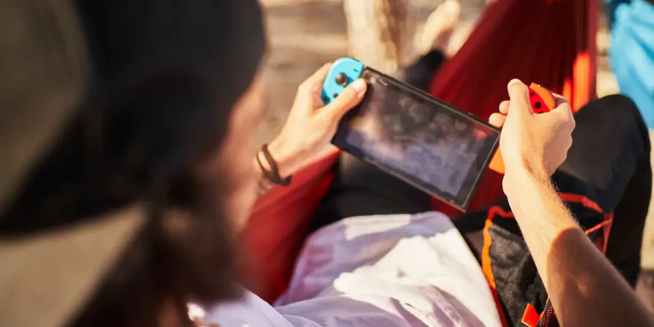 Osoba w hamaku gra na Nintendo Switch. Czas ładowania konsoli jest krótki, więc można grać wszędzie.