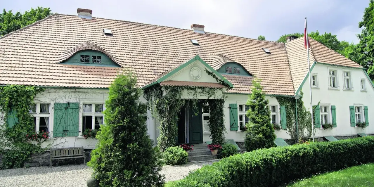 Urokliwy dwór Wybickich z zielonymi okiennicami i pnączami.