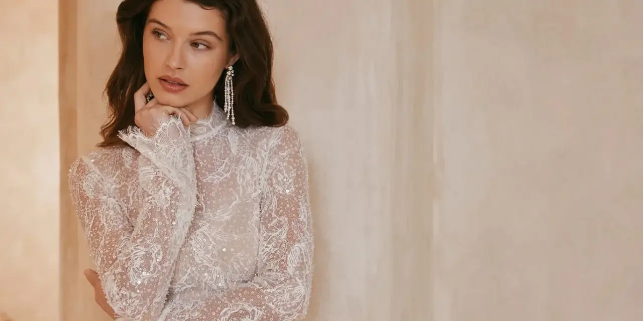 Elegancka, biała sukienka bez dekoltu, zdobiona koronką i cekinami, z długimi rękawami.