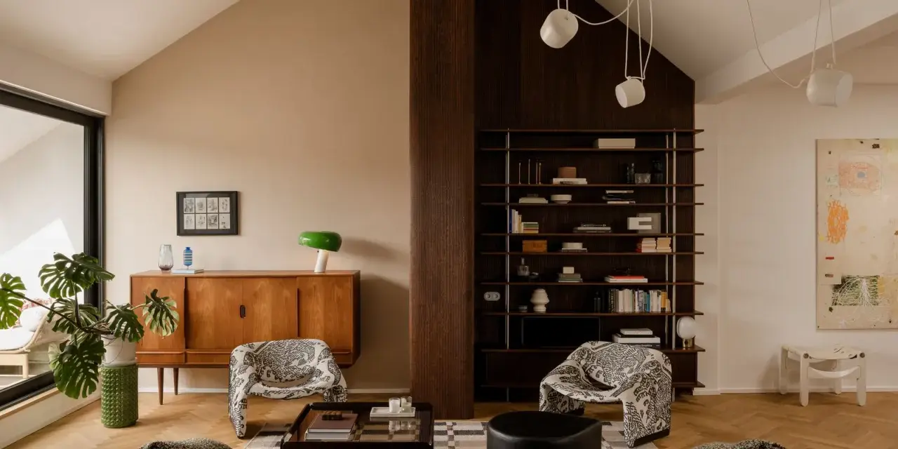 Salón acogedor con **techo inclinado interior**, muebles de madera, estanterías y sillones estampados.
