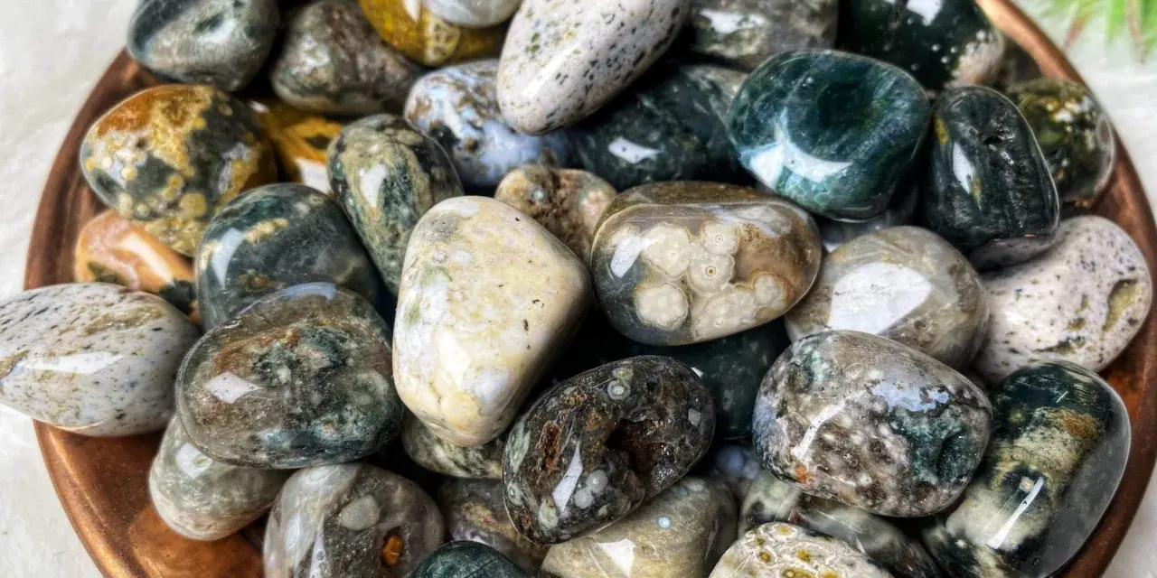 Montón de piedras jaspe blanco pulidas, con vetas verdes, marrones y amarillas. Sus propiedades son conocidas por su conexión con la naturaleza.