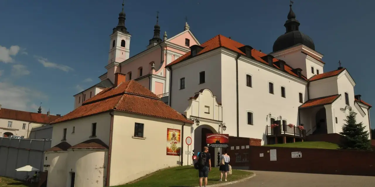 Białe budynki z czerwonymi dachami, wieże i kopuła tworzą malowniczy klasztor kamedułów.