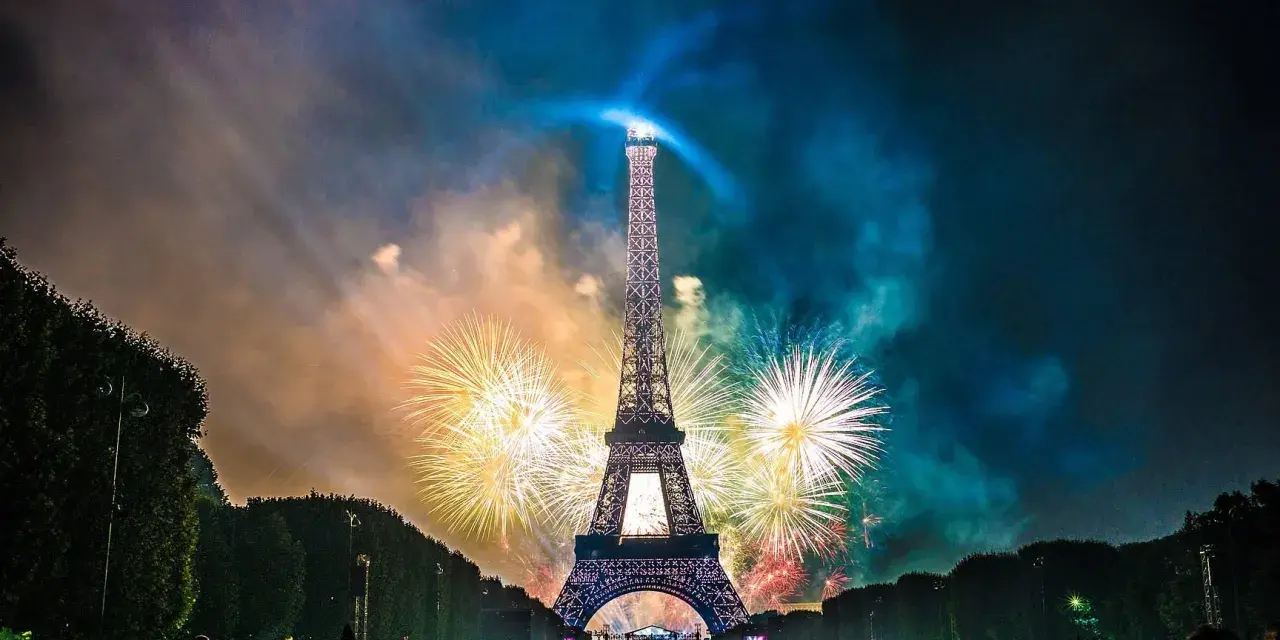 Espectacular espectáculo de fuegos artificiales ilumina la Torre Eiffel, celebrando porque se celebra el 14 de julio en Francia. Multitud observa.