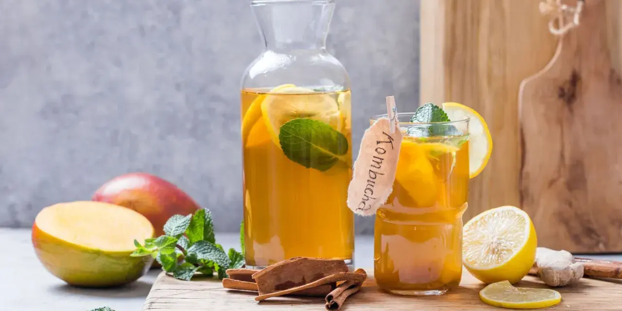 Verre et carafe de kombucha thé rafraîchissant avec des tranches de citron, de la menthe, des bâtons de cannelle et des mangues.