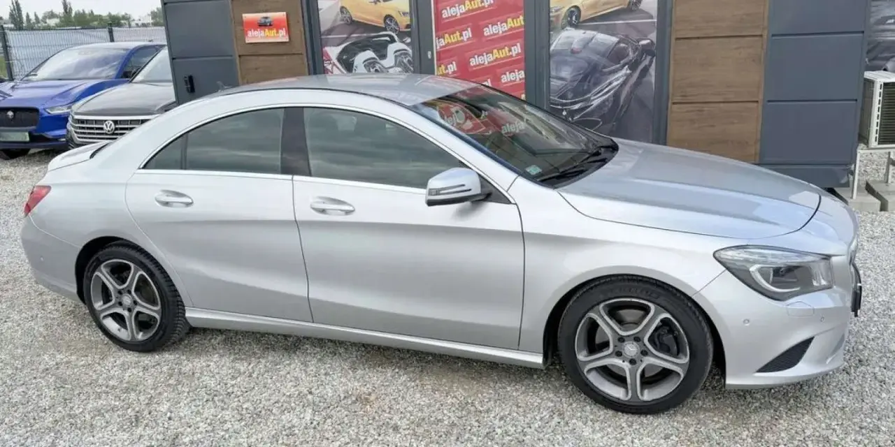 Srebrny Mercedes CLA na tle salonu samochodowego z reklamami.