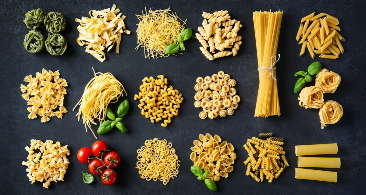 Różnorodne włoskie dania z makaronem: od tagliatelle i spaghetti po farfalle i penne, z dodatkiem pomidorków i bazylii.