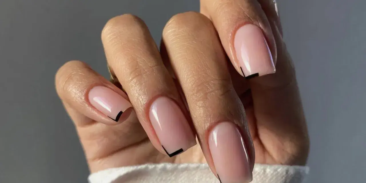 Mano con unghie quadrate naturali, smalto rosa tenue e un sottile dettaglio grafico nero sulla punta.