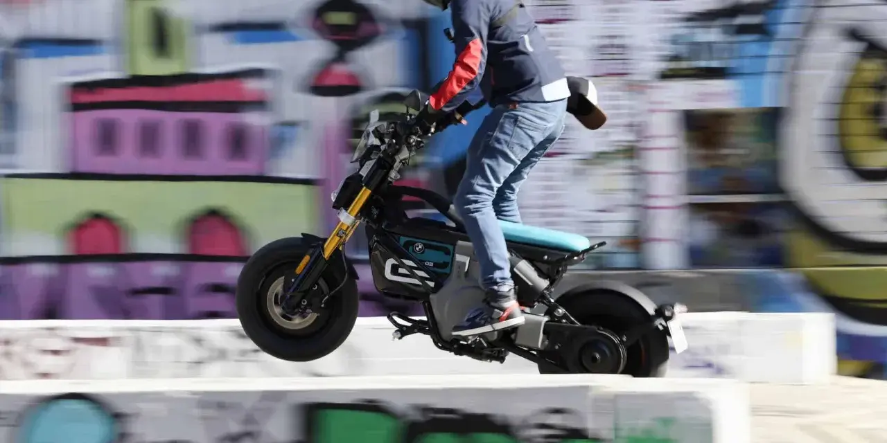 Młody mężczyzna na elektrycznym motocyklu BMW CE02 wykonuje skok na tle kolorowego graffiti.