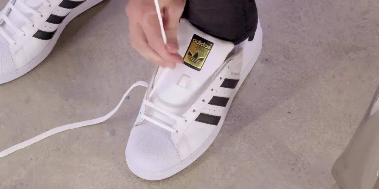 Pokazuję, jak wiązać sznurówki w adidasach Superstar. Białe sznurówki przeplatane przez czarne paski.
