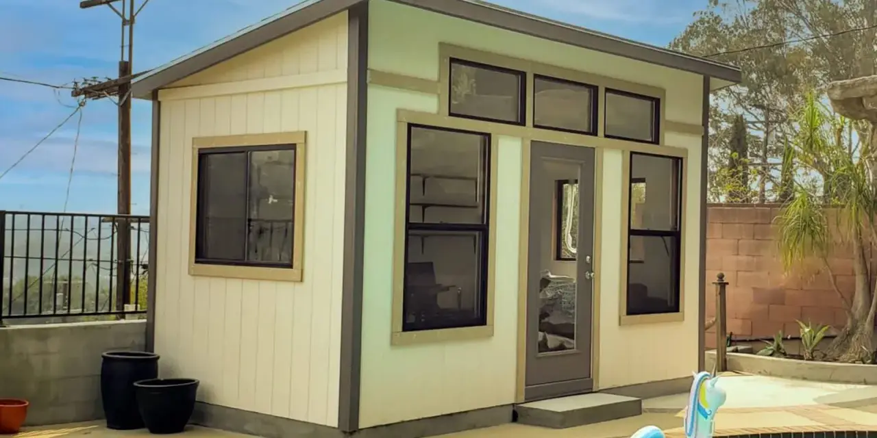 A modern shed, perfect to build a backyard oasis, sits by a pool with a unicorn float.