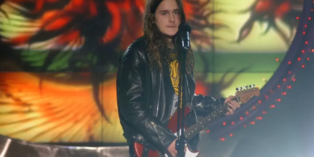 Zalewski w Idolu, z gitarą i w skórzanej kurtce, na tle kolorowej scenografii.
