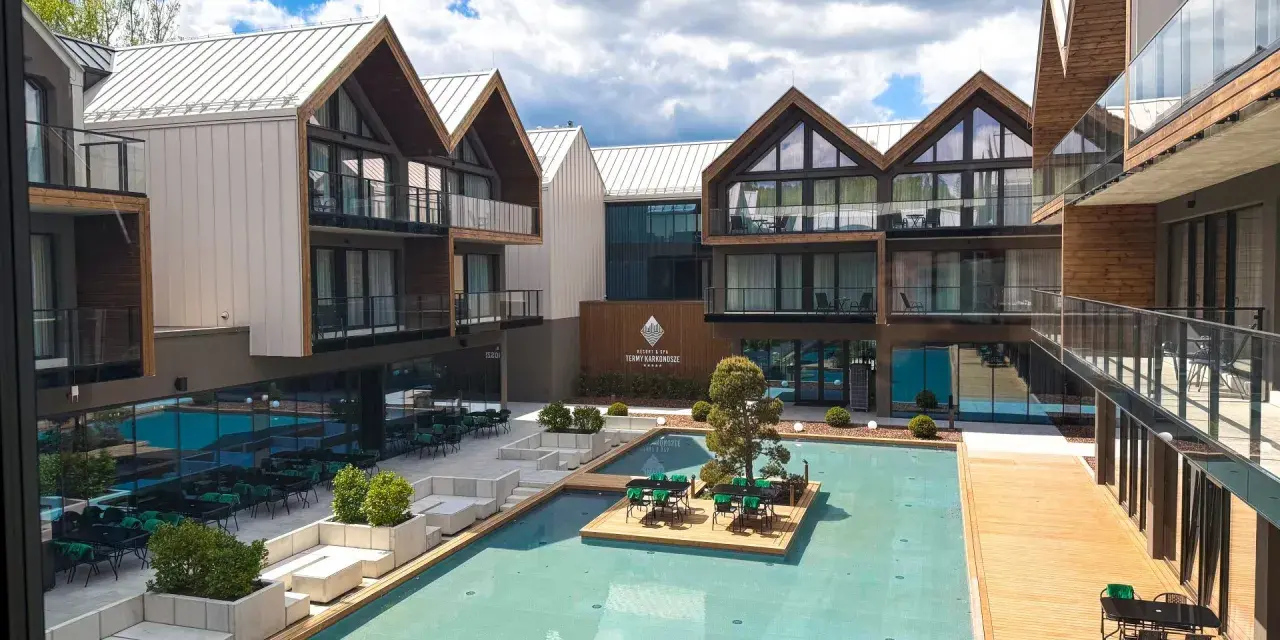 Nowoczesny hotel z basenem i tarasami. W centralnym punkcie basen z wyspą i stolikami, otoczony budynkami z drewnianymi elementami. Idealne miejsce na wypoczynek, jak w bajkowym jagniątkowie.