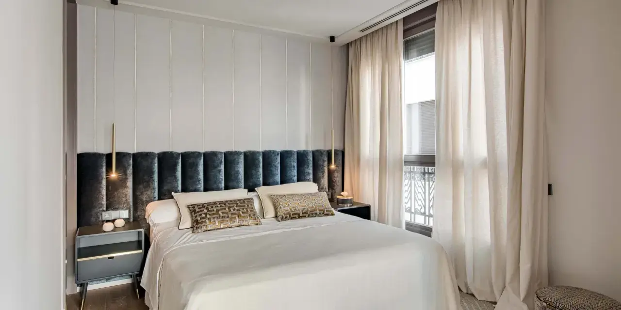 Acogedora habitación pequeña con cama grande, cabecero tapizado, mesitas de noche modernas y cortinas elegantes.